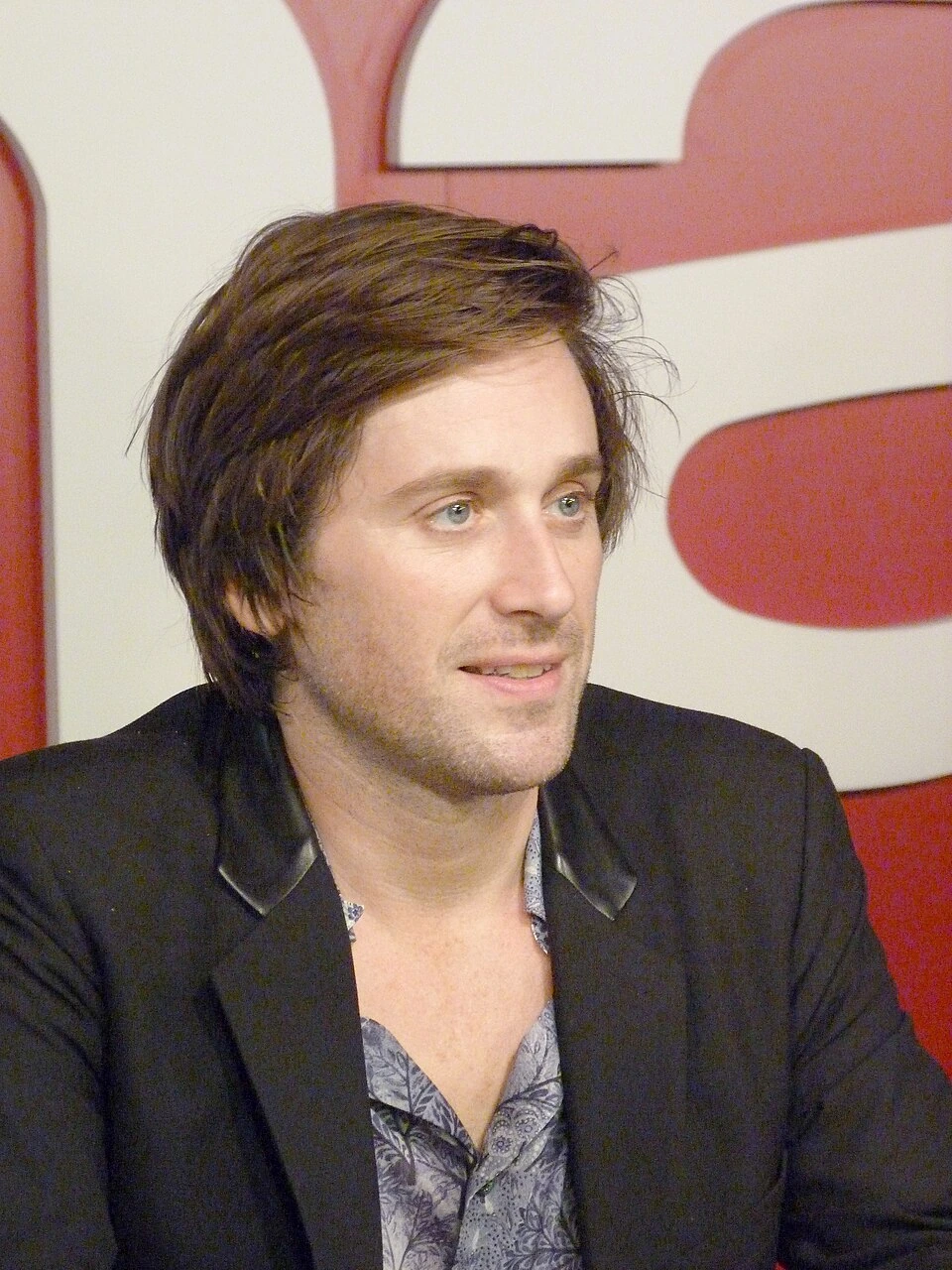 Thomas Dutronc en portrait lors d’un événement, en veste sombre devant un fond rouge et blanc.